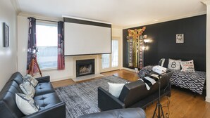 A living room with a black leather sofa, a black and white patterned rug, a fireplace, a bed with patterned bedding, and a projector screen. - Movie Nights Nash! 2bd Townhome off WEST END! 8 min-> DT! (Nashville)