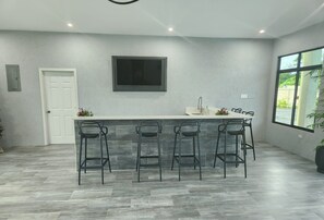 A modern kitchen with a bar area, grey tiled flooring, and a large window providing natural light.