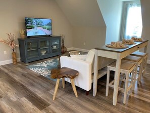 A dining area with a wooden table, white chairs, and a television on a cabinet. - Welcome to the Cape! Cute, quiet and clean apartment ready for your stay. (Bourne)