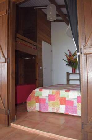 A bedroom with a wooden bed frame, a quilt, and a small bedside table with a vase of flowers.