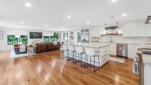 Une cuisine moderne avec des meubles blancs, un plancher en bois et un coin bar équipé de tabourets.