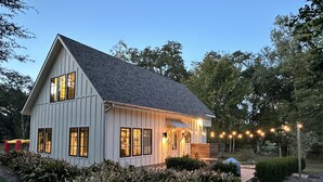 Une maison blanche à deux étages, dotée d’un toit en pente, de grandes fenêtres et d’un porche.