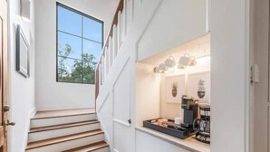 Un escalier mène à un coin cuisine équipé d’une machine à café et agrémenté d’une plante posée sur le comptoir.