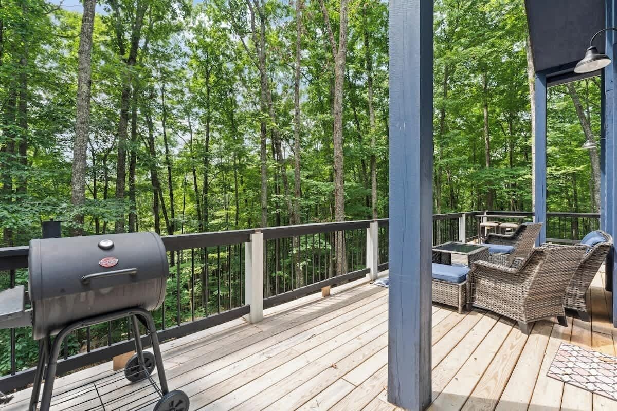 A deck with a grill, wicker furniture, and a view of a forest.