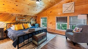 A cozy cabin with a wooden interior, a bed with a blue bedspread, a chest of drawers, a chair, and a ceiling fan. - 3BR 2BA w/ King Bed/Hot Tub in Heart of RRG (Campton)