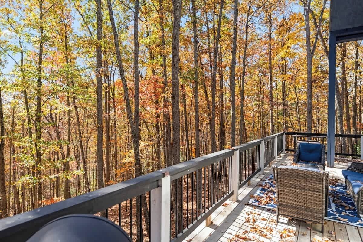 Une terrasse en bois, dotée de meubles en osier et d’une balustrade donnant sur une forêt.