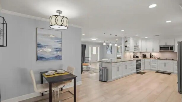 A modern kitchen with white cabinets, a central island, and a dining area with a table and chairs. - Luxury Ranch 2 Master Kg Bed w/ heated Salted Pool (Orlando)