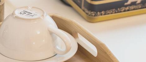 A white teapot on a wooden tray with a box of snacks in the background.