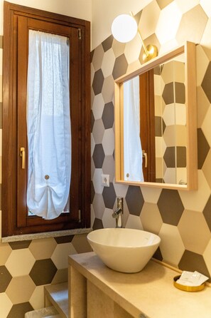 Un baño con puerta de madera, un lavabo blanco, un espejo y pared con estampado geométrico.