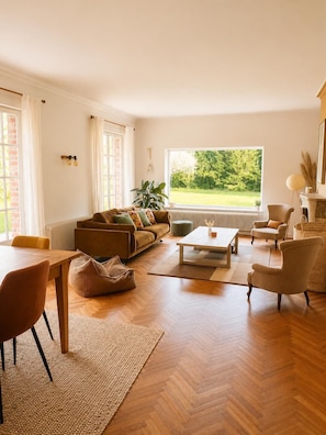 A living room with a sofa, coffee table, chairs, a dining table, and a view of greenery outside. - les jardins de Beaumont (Hem)