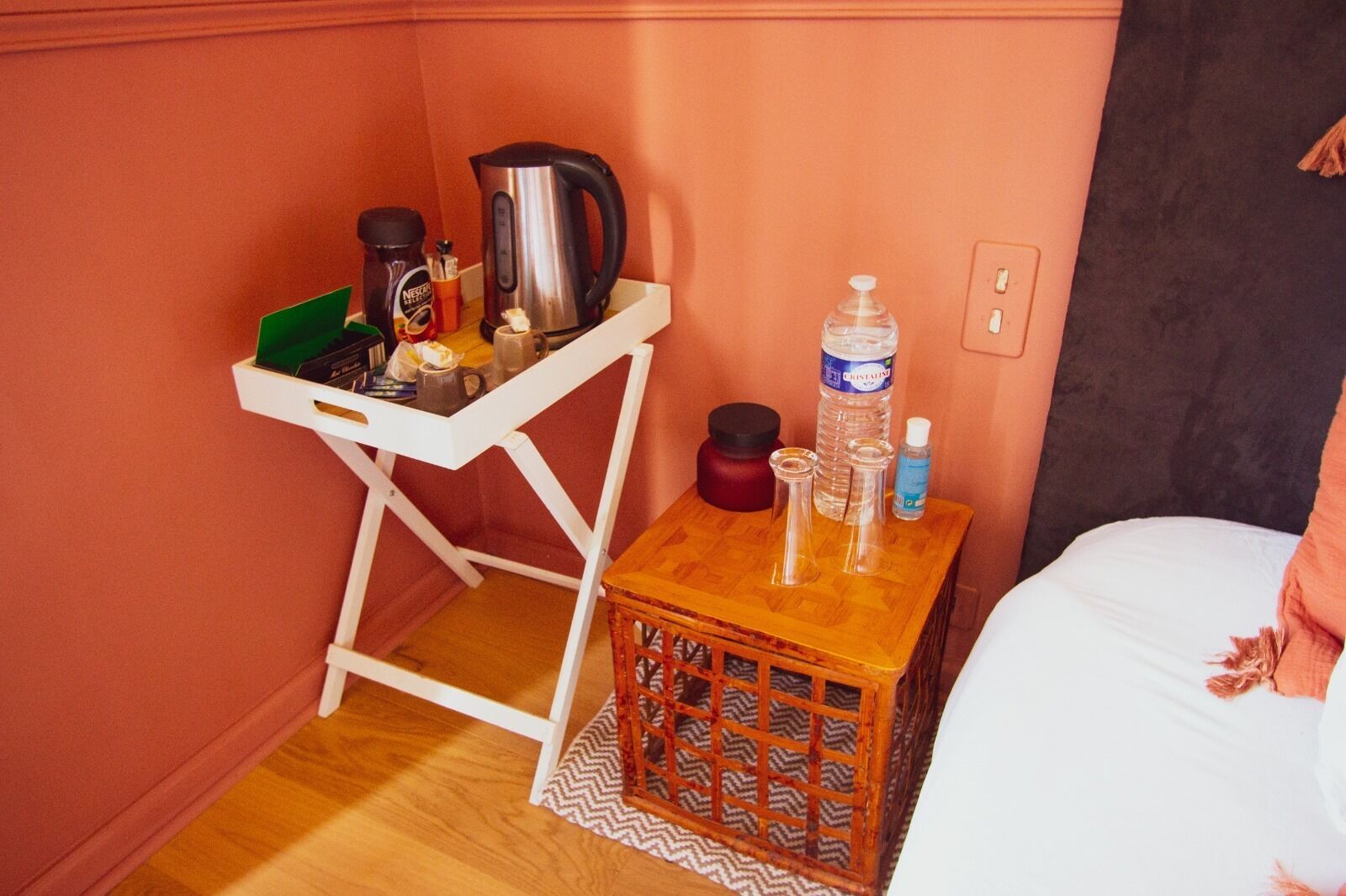 Een kleine kamer met een wit bureau, een houten nachtkastje, een bed en een stopcontact.