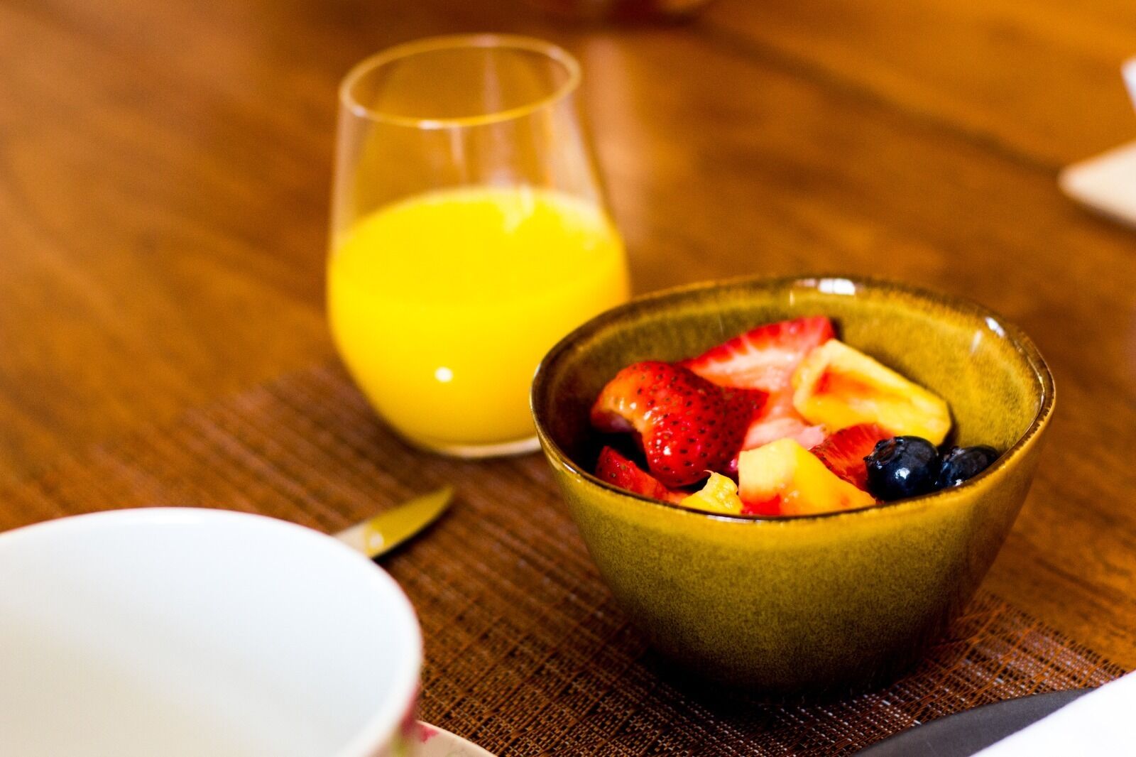 Una mesa de madera con un bol de fruta y un vaso de zumo de naranja.