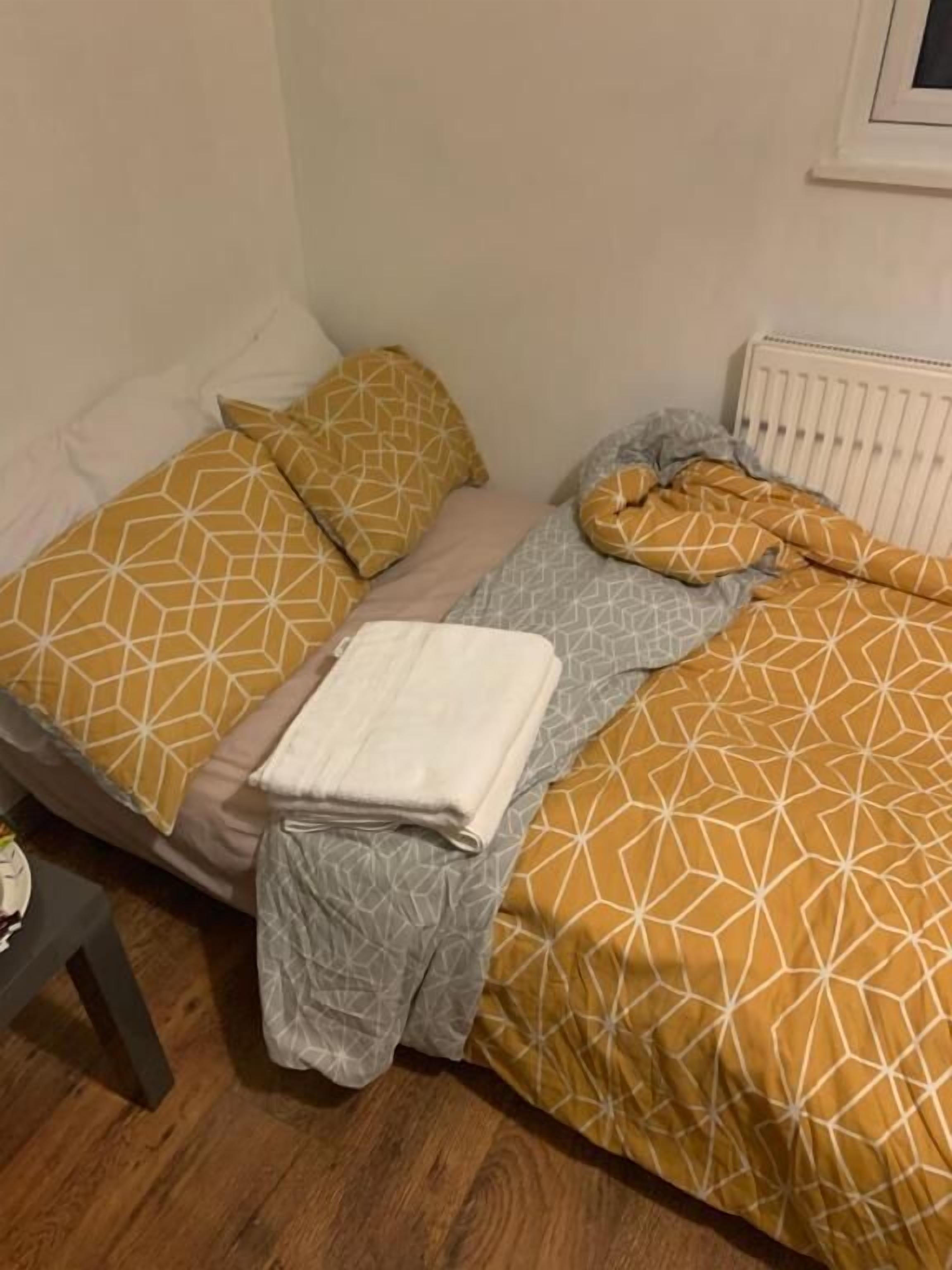 A small, simple room with a bed, a radiator, and a wooden floor.