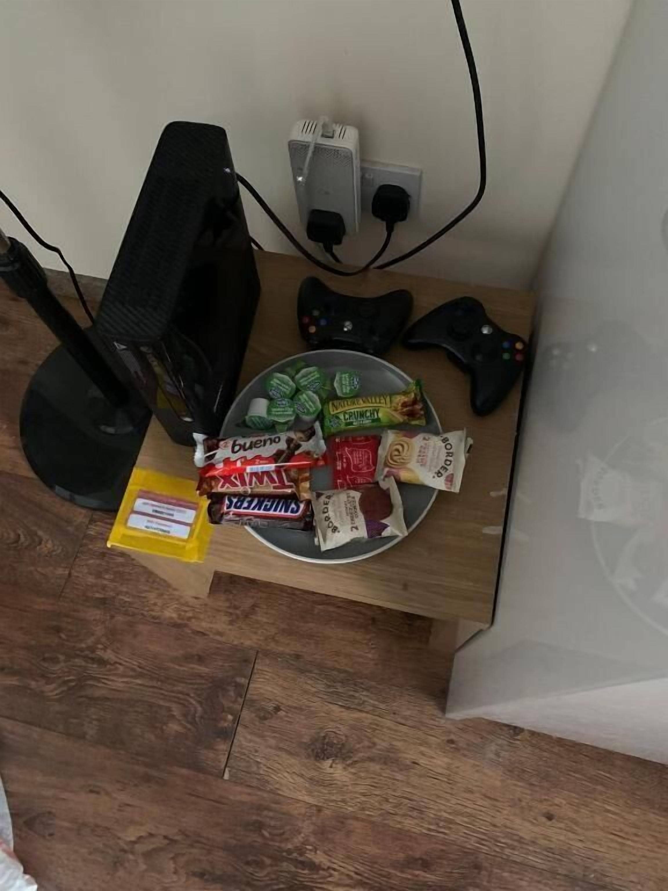 Een houten tafel met een bord met snacks, een televisie en een gamecontroller.
