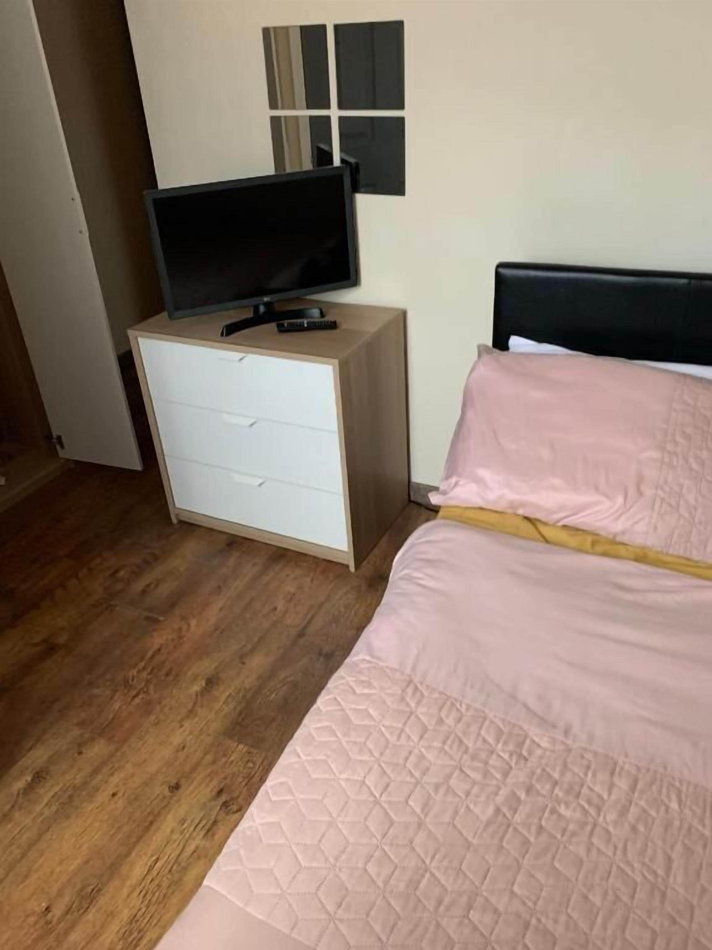 A bedroom with a bed, a nightstand, a television, and a wall-mounted mirror.