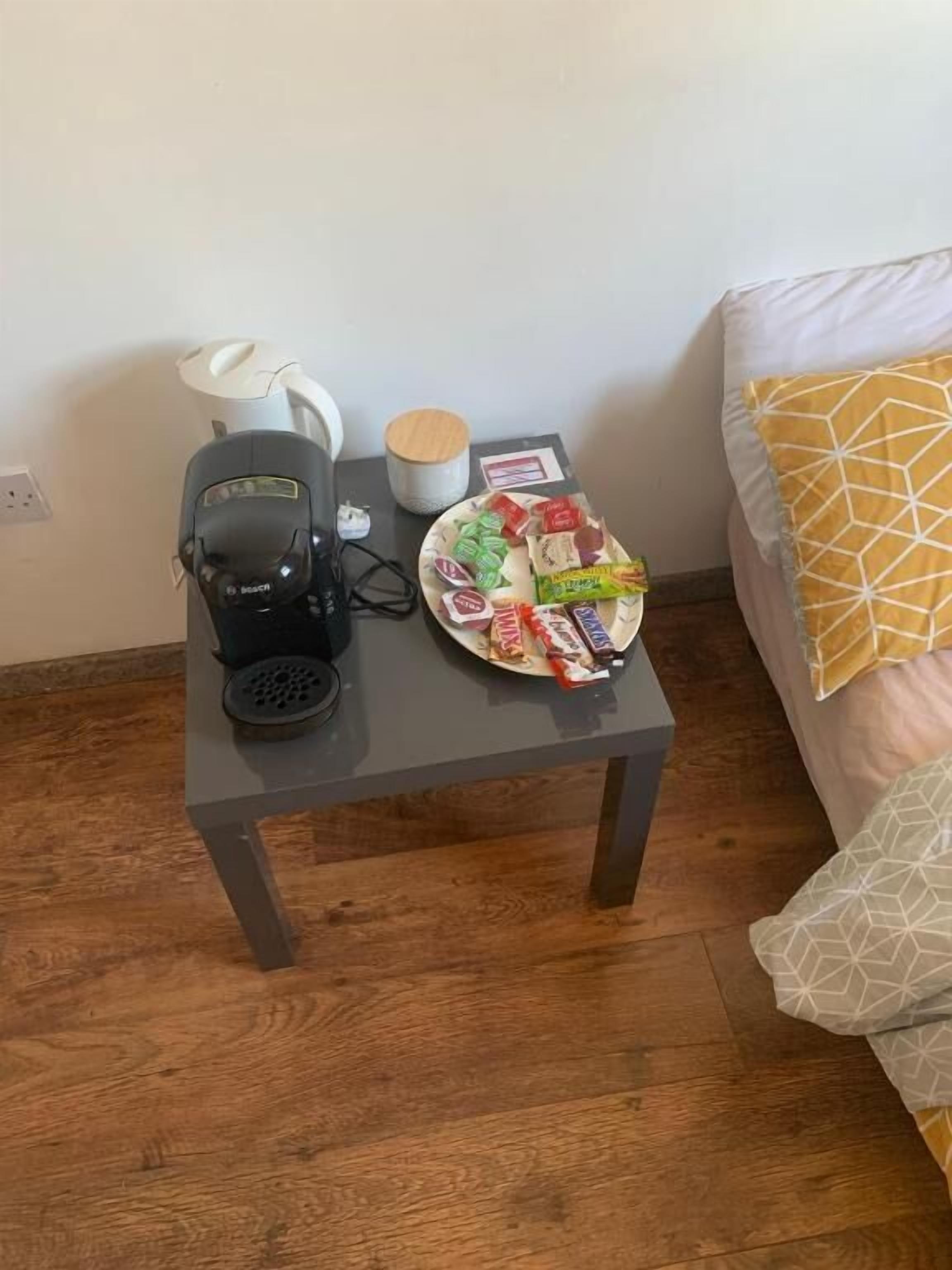A small table with a coffee maker, a plate of snacks, a candle, and a small container.