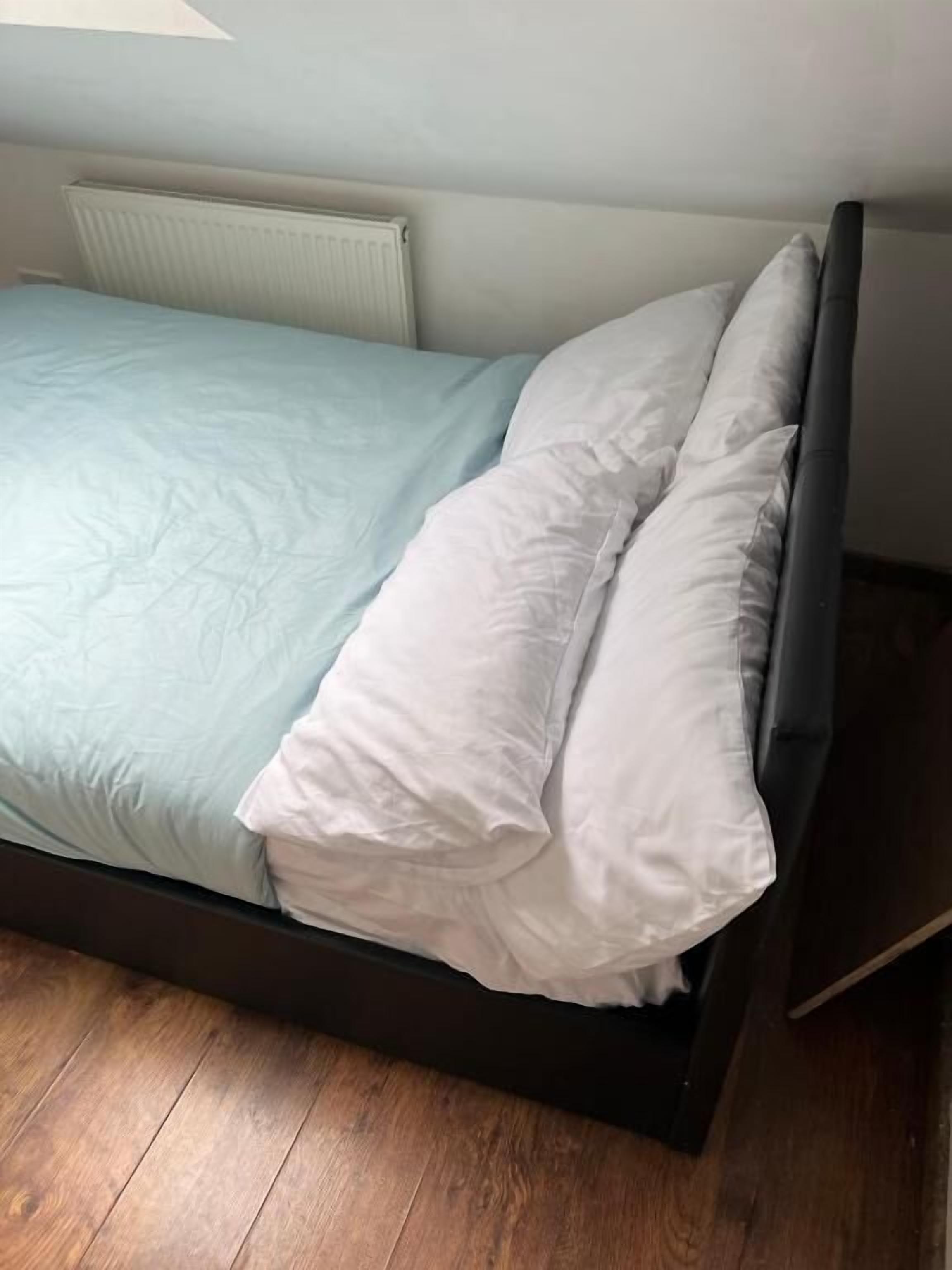A bed with a light blue bedspread and white pillows, a dark headboard, and a white radiator above it.
