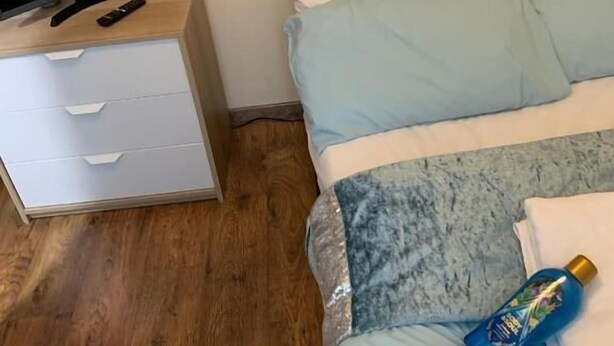 Un dormitorio con una cama, un televisor sobre un aparador de madera y una botella sobre la cama.