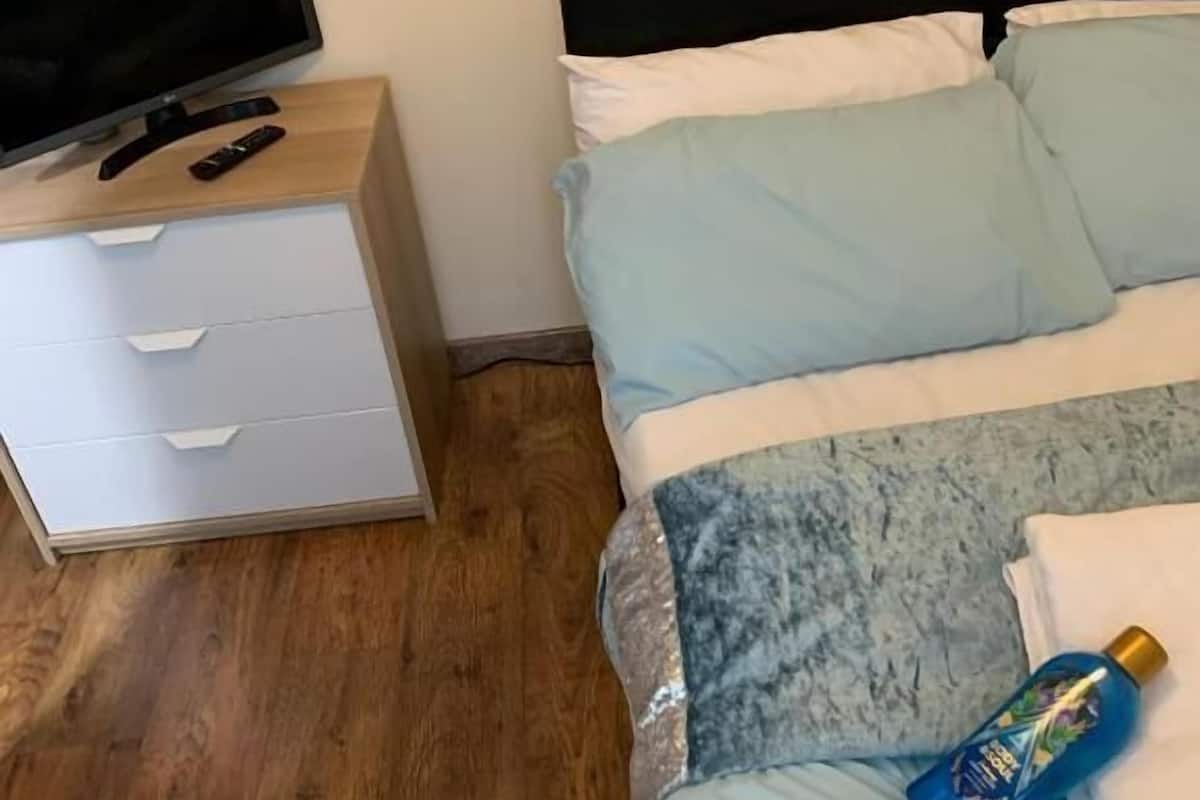 A bedroom with a bed, a TV on a wooden dresser, and a bottle on the bed.