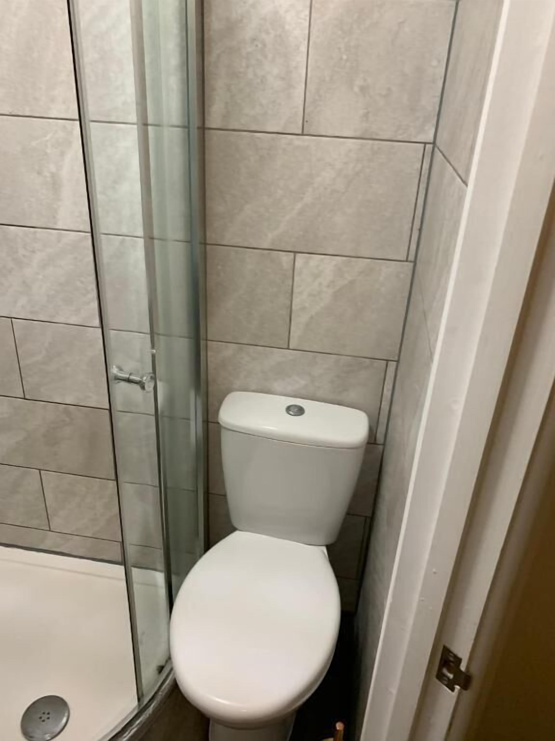 A bathroom with a toilet, a glass shower enclosure, and tiled walls.