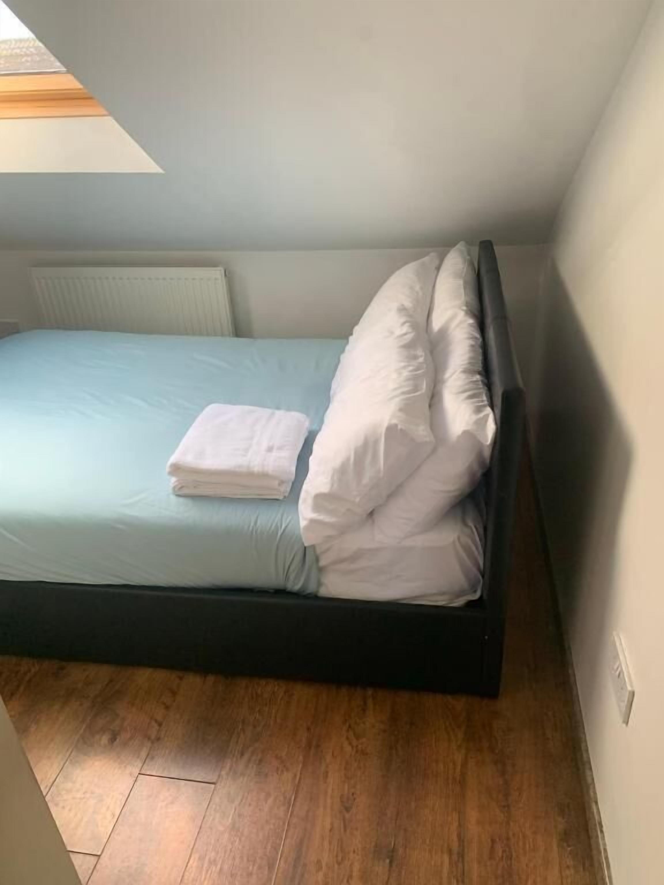 A small, single-bed room with a wooden floor, light blue bedding, and a white pillow.