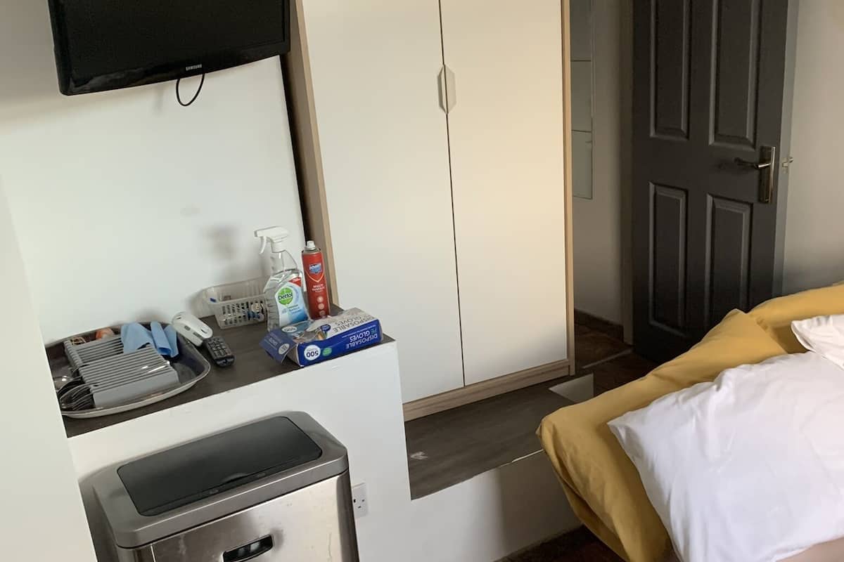 A hotel room with a bed, a small kitchenette, a TV mounted on the wall, and a door leading to another room.
