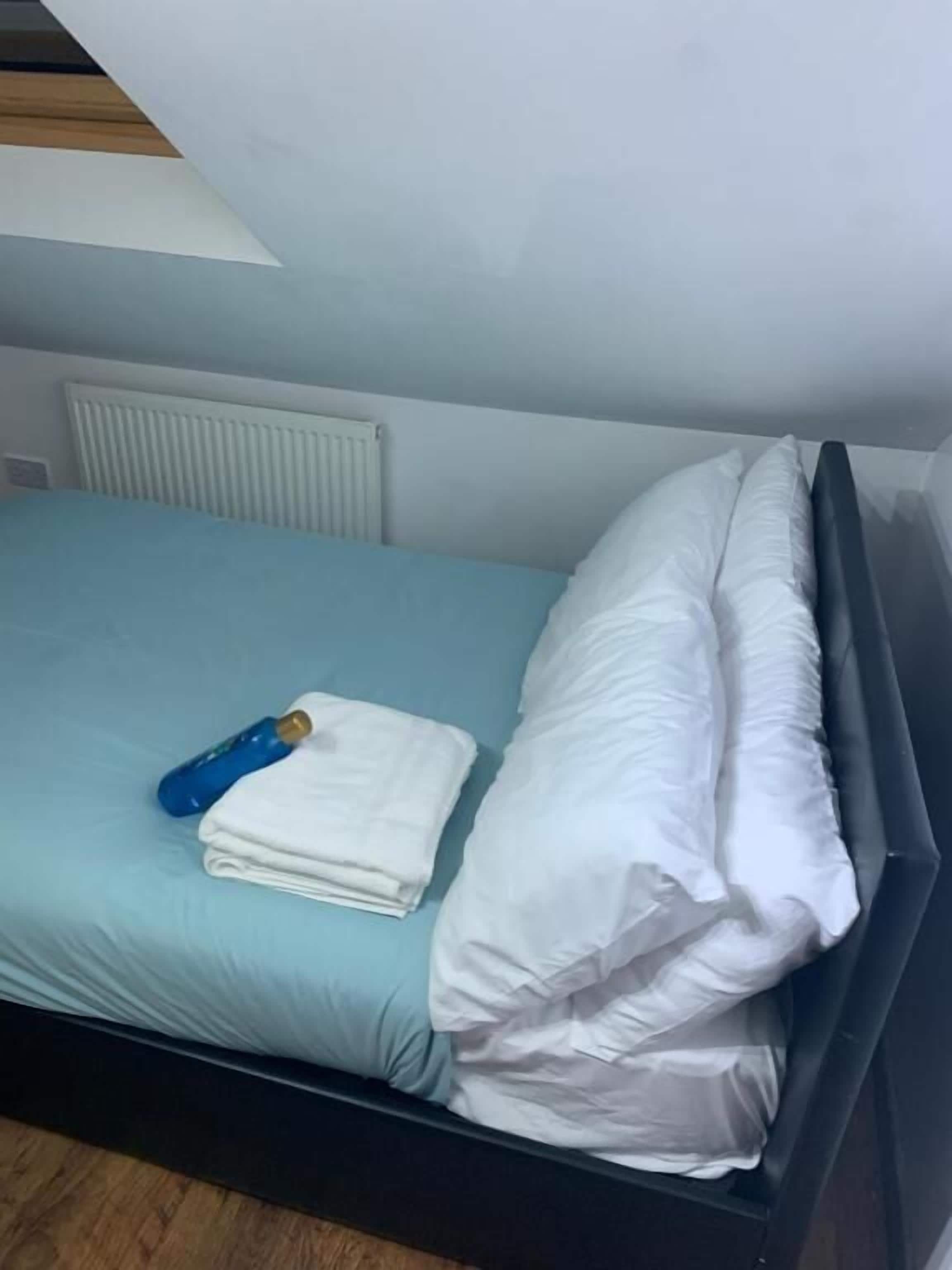 Una habitación pequeña con cama individual, colchón azul, almohadas blancas y una botella azul.