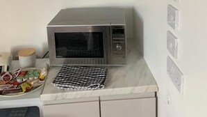 Una cocina compacta con microondas incorporado y repisas superiores con vasos y vajilla.
