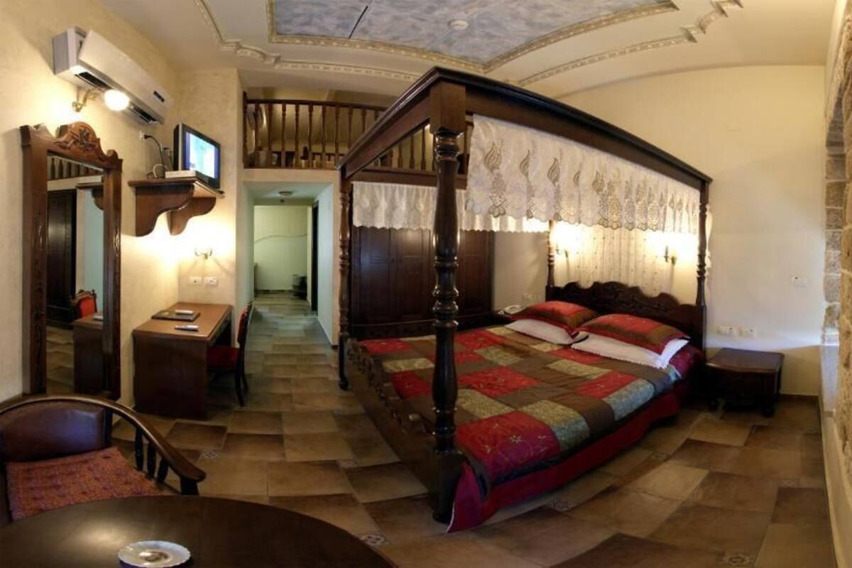 Een slaapkamer met een hemelbed, een houten bureau, een stoel en een televisie op een plank.