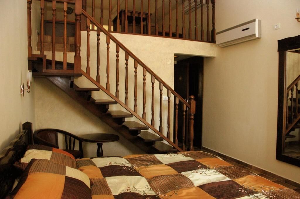 A bedroom with a wooden staircase, a bed with a quilt, a chair, and a small table.