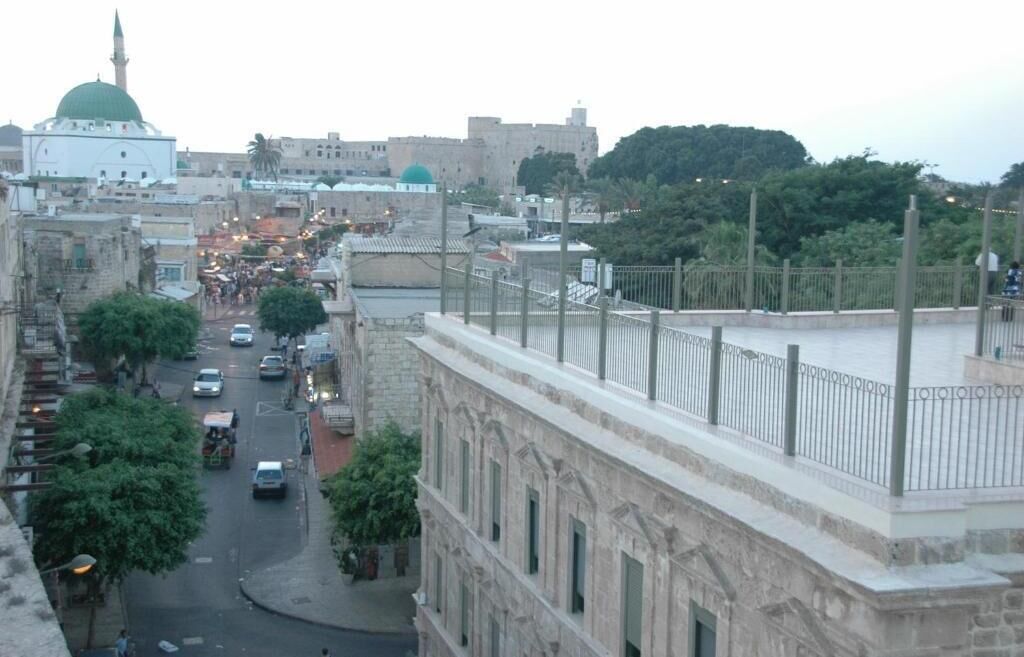 Vista d'un carrer amb edificis, una mesquita amb cúpula verda i una tanca que faiguer a l'avinguda.
