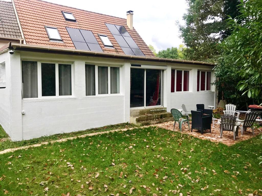 A house with a sloped roof, solar panels, a covered patio with chairs, and a lawn with fallen leaves.