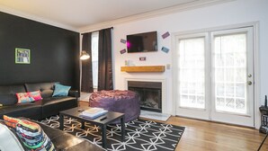 A living room with a black sofa, a coffee table, a fireplace, and a television. - 90's in Nash! 2bd Townhome in WEST END! 8 min ->DT! (Nashville)