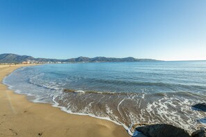 A beach with clear blue water, a sandy shore, and distant mountains.