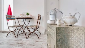 A room with a dining table, chairs, a coffee machine, a teapot, and a cabinet.