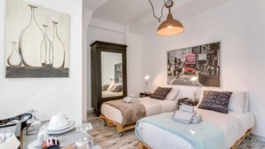 A room with two beds, a dining table with plates and glasses, a hanging lamp, and artwork on the walls.
