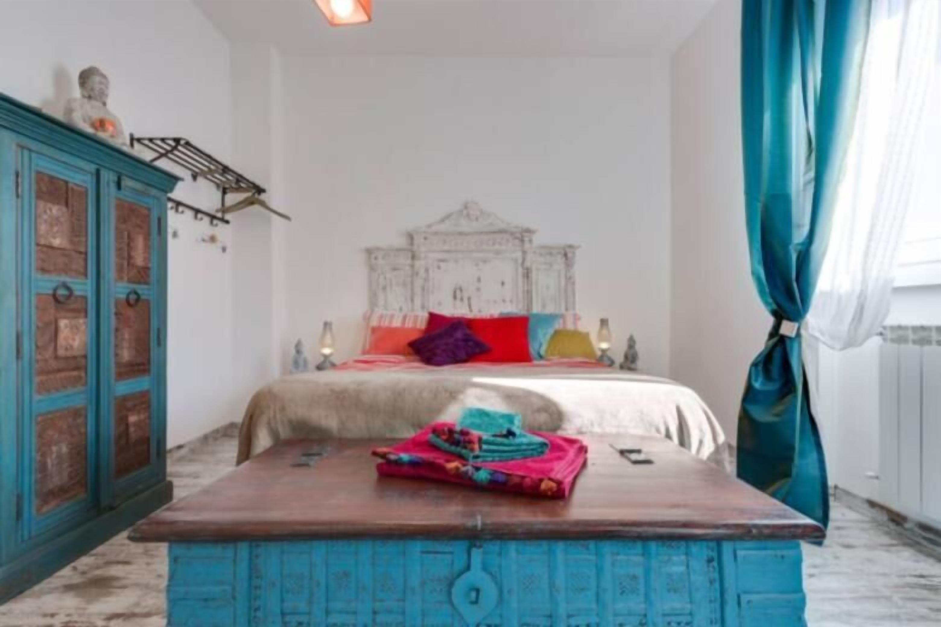 Une chambre à coucher avec un lit, une commode bleue et une étagère murale sur laquelle est posée une statue.