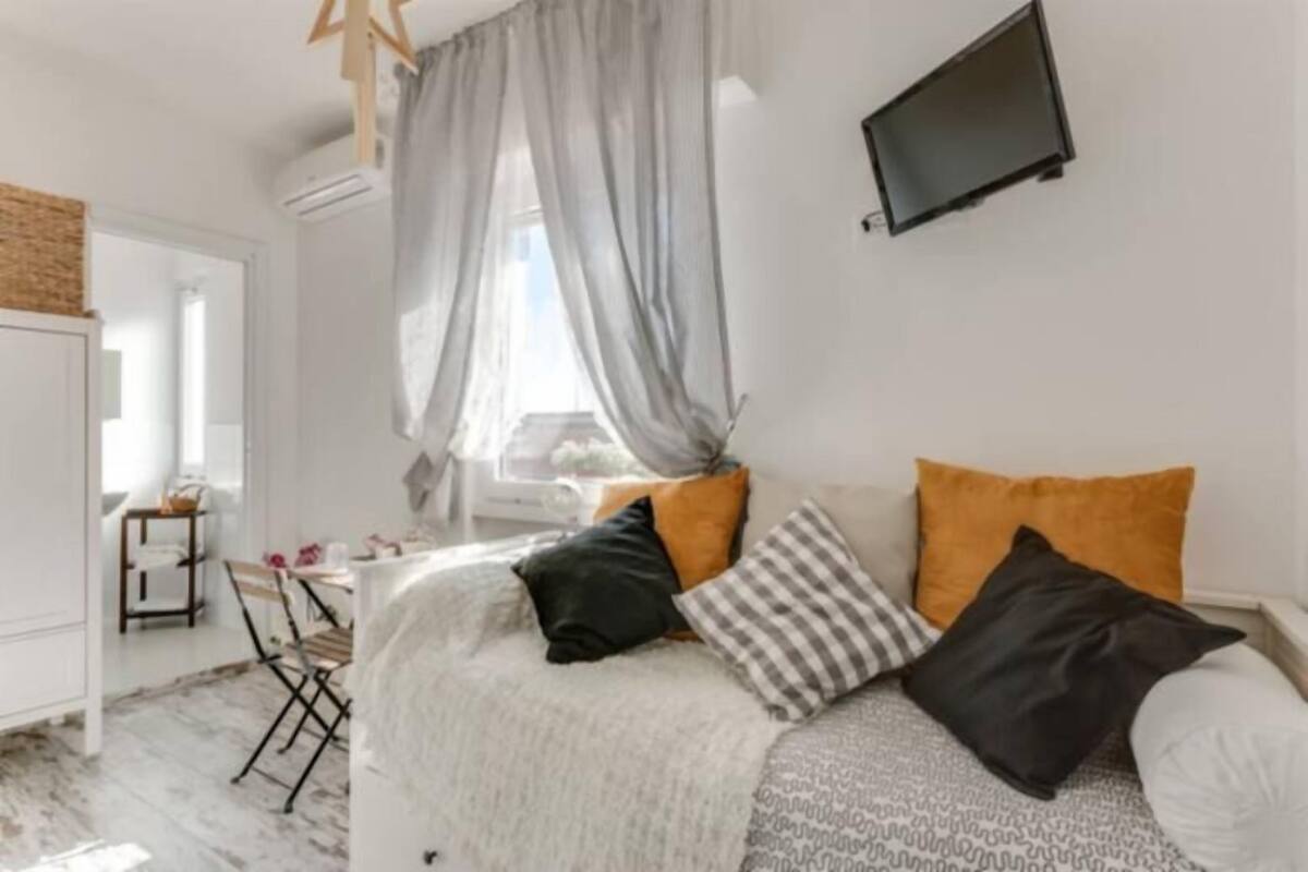 A bedroom with a bed, a TV mounted on the wall, and a window with sheer curtains.