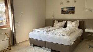Un lit bien fait, avec une tête de lit, une table de chevet sur laquelle se trouve une lampe, et un tableau accroché au mur.