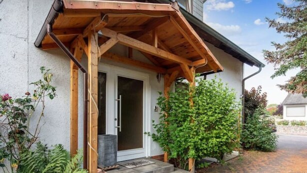 Une maison avec un porche en bois, une porte et un petit jardin où poussent différentes plantes.