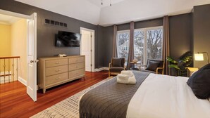 Une chambre à coucher avec un lit, une commode, un téléviseur, une chaise et une fenêtre avec des rideaux.
