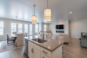 A modern kitchen with a central island, pendant lights, and a stone fireplace.