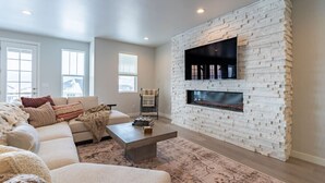 A modern living room with a white brick fireplace, a sofa, and a coffee table. - NEW 3BR Luxury Townhome (Heber City)