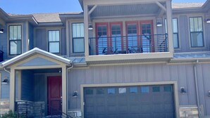 A two-story house with a red front door, a garage, and a balcony with outdoor furniture. - NEW 3BR Luxury Townhome (Heber City)