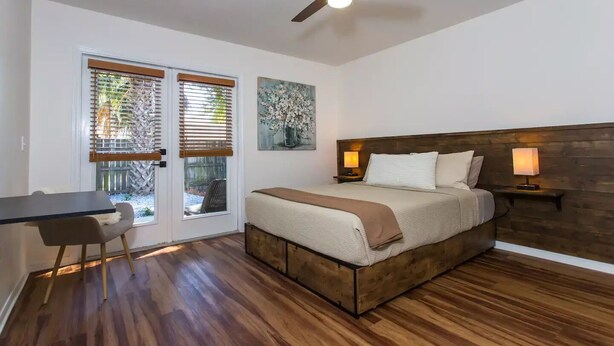 Un dormitorio con una cama de madera, dos l ámparas de noche, un ventilador de techo y un escritorio con una silla.