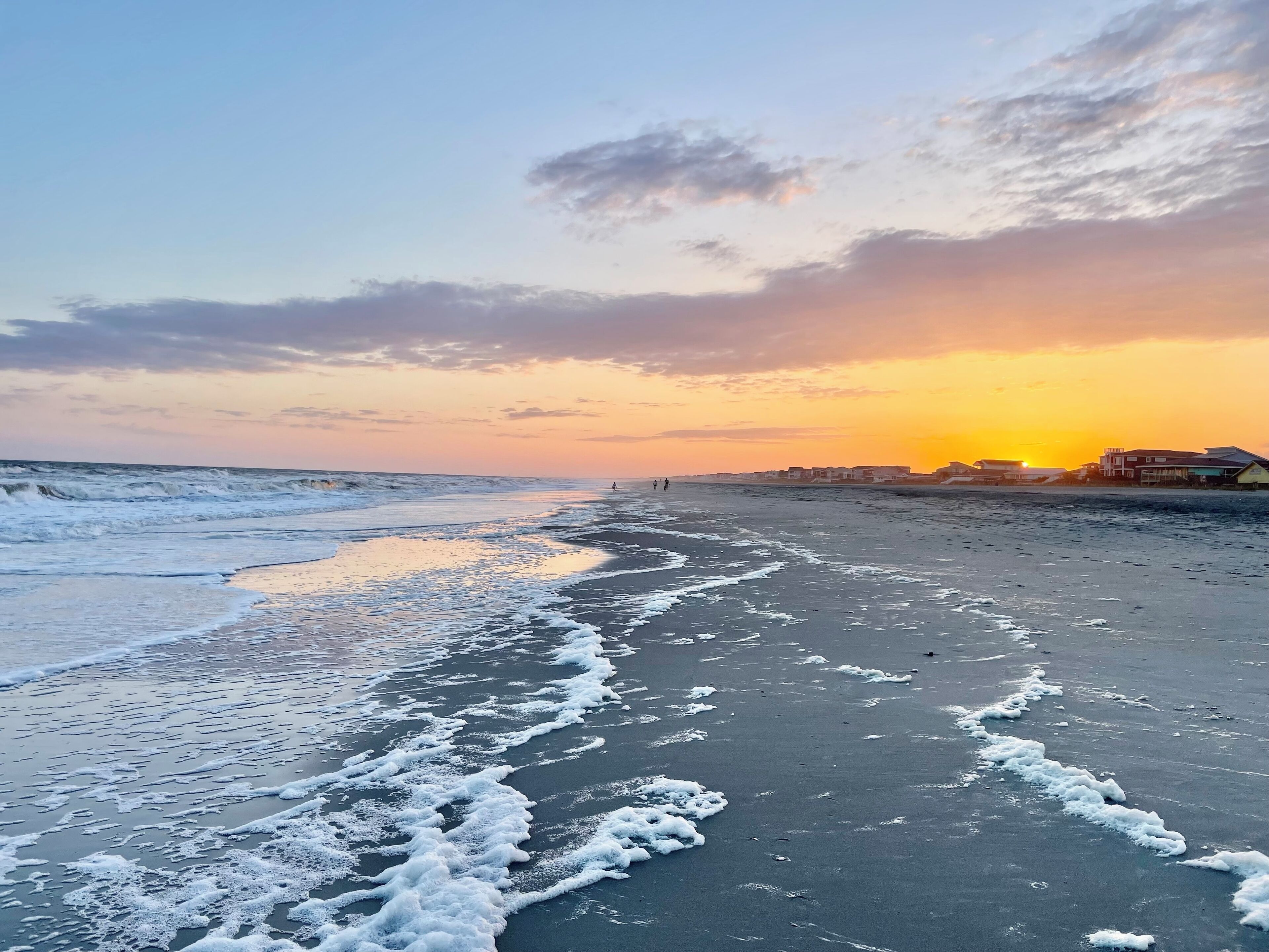 A beach with waves, a sunset, and buildings in the background. - Premiere Location! Canal Front, Dock, Easy Beach & Pier Access (Holden Beach)