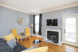 A living room with a grey couch, yellow armchairs, a fireplace, and a TV mounted on the wall.