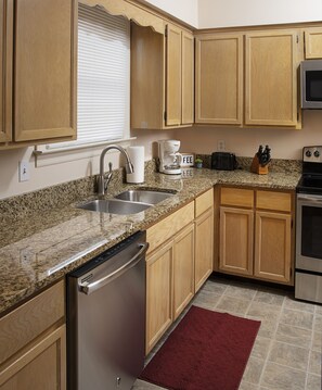 A kitchen with wooden cabinets, a granite countertop, a dishwasher, a coffee maker, a toaster, and a stove.