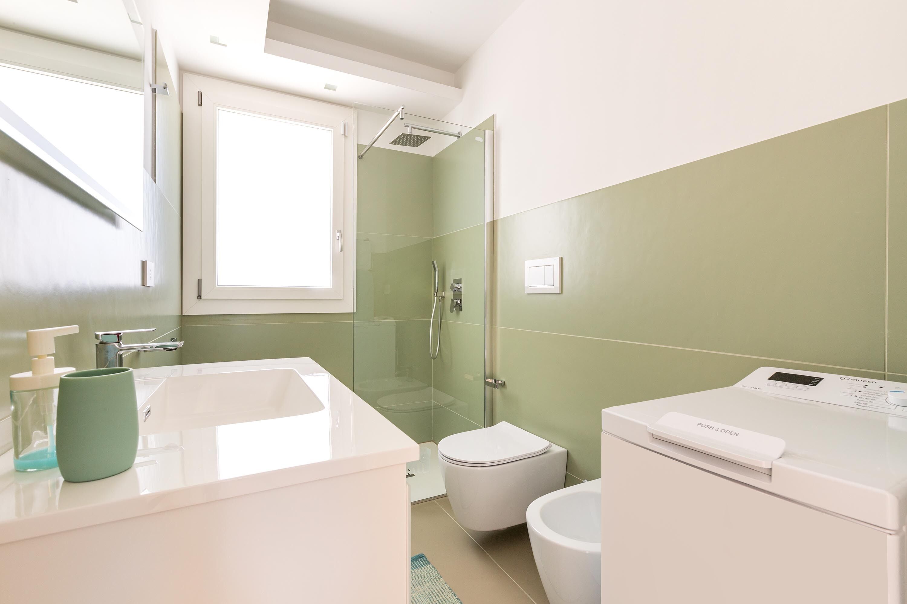 A modern bathroom with a glass-enclosed shower, a white sink, and a washing machine.