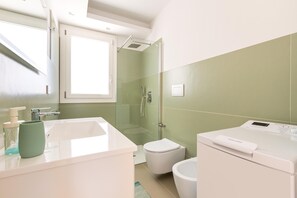 Un baño moderno con ducha envuelta en vidrio, un lavamanos blanco y una lavadora.